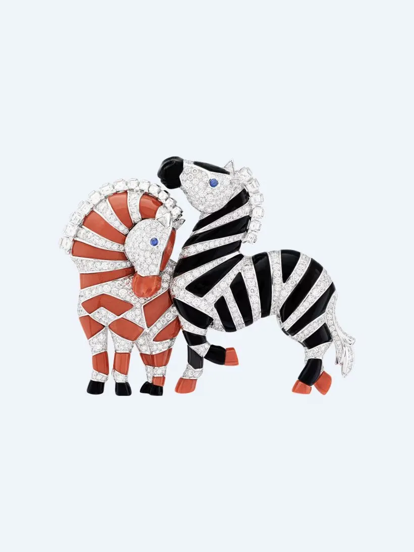 Pırlanta detaylarla süslenmiş siyah-beyaz çizgili zebra ve turuncu mercan tonlarında yeleli aslan figürlerinden oluşan, mine kaplamalı lüks broş tasarımı.