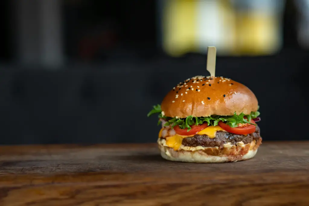 Taze domates, yeşillik ve cheddar peynirli sulu cheeseburgerin ahşap masa üzerindeki iştah açıcı yakın çekimi.