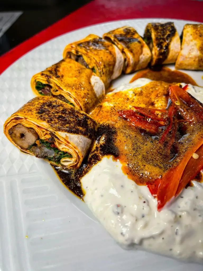 Yoğurt ve domates sosuyla sunulmuş beyti kebabı dilimleri.