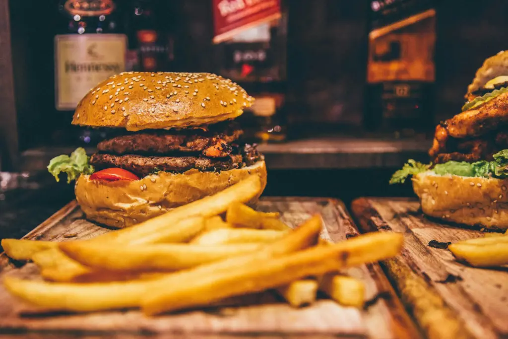 Patates kızartması eşliğinde iki katlı burger ve arka planda viski şişeleri.