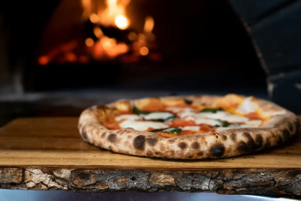 Odun fırınında pişmiş Napoli tarzı pizza, arka planda yanan ateş.