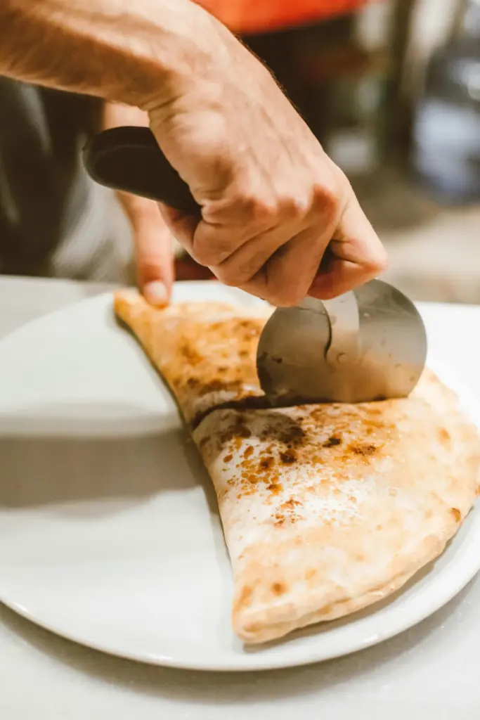 Pizzayı kesen bir elin yakın çekimi; rustik ve romantik restoran ortamı hissi