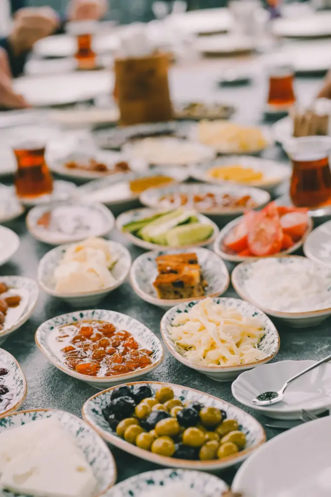 Geleneksel Türk kahvaltısı; çeşitli peynirler, zeytinler, reçeller, domates, salatalık ve çay bardaklarıyla dolu uzun bir masa üzerinde servis edilmiş renkli ve iştah açıcı kahvaltılıklarla donatılmış bir sofra.