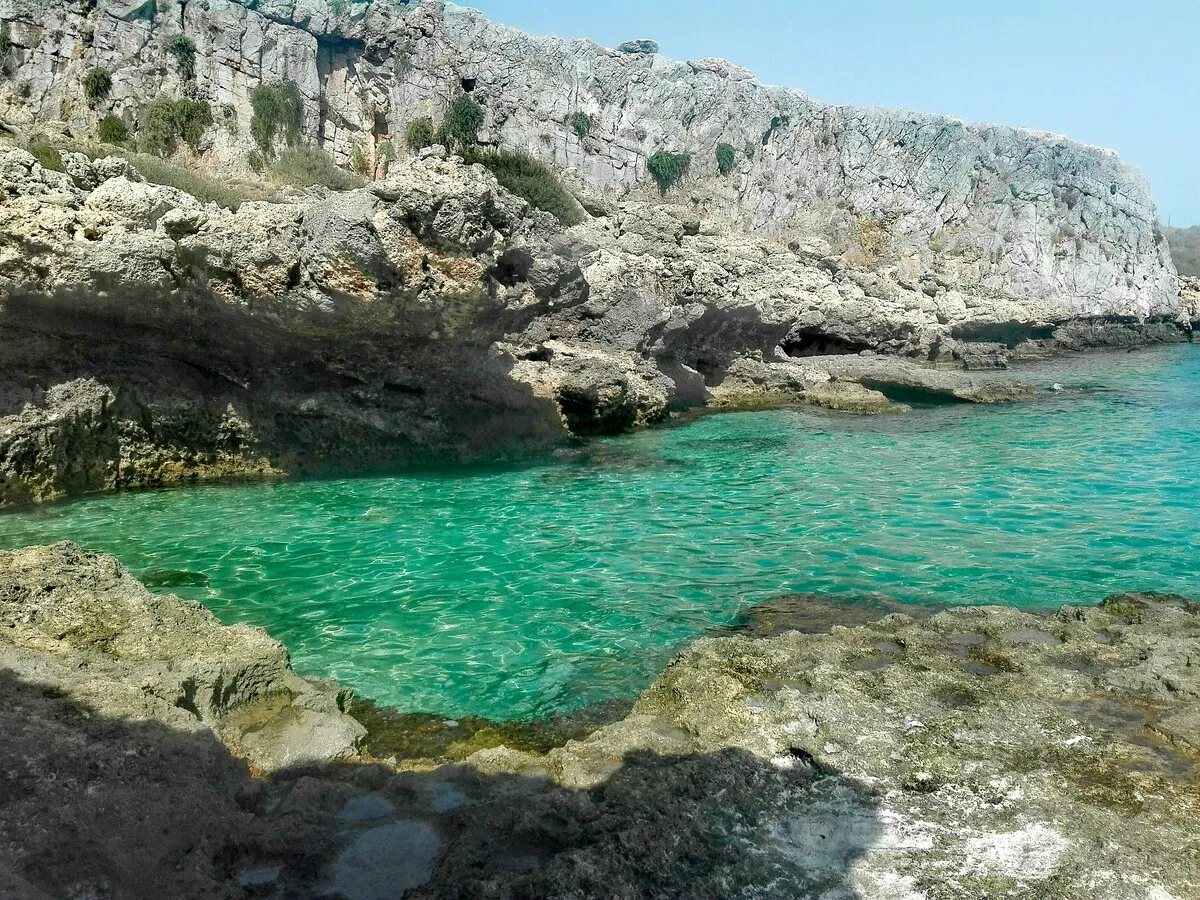 Rodos, Yunanistan'da, güneşli bir günde, etrafı girintili çıkıntılı gri kayalıklarla çevrili, pırıl pırıl turkuaz renkli berrak sularıyla dikkat çeken doğal bir koyun huzur veren manzarası.