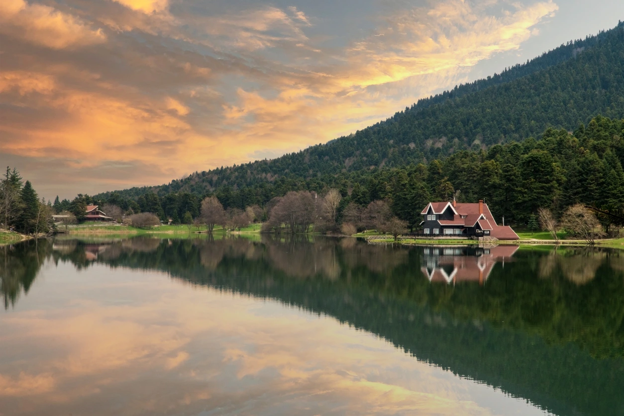 Bolu Abant Gölü'nün sakin sularının yemyeşil ağaçları ve bulutlu gökyüzünü berrak bir şekilde yansıttığı, doğanın tüm güzelliklerini cömertçe sergilediği bu büyüleyici manzara, ziyaretçilerine unutulmaz bir huzur sunuyor.