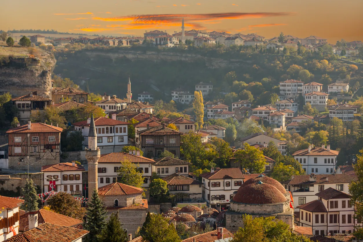 Safranbolu'nun yamaçlarda konumlanan, kırmızı kiremitli çatılara ve beyaz badanalı ahşap cephelere sahip, yeşil doğayla iç içe geçmiş geleneksel Osmanlı evlerinin masmavi gökyüzü altındaki büyüleyici ve ikonik panoramik görüntüsü.