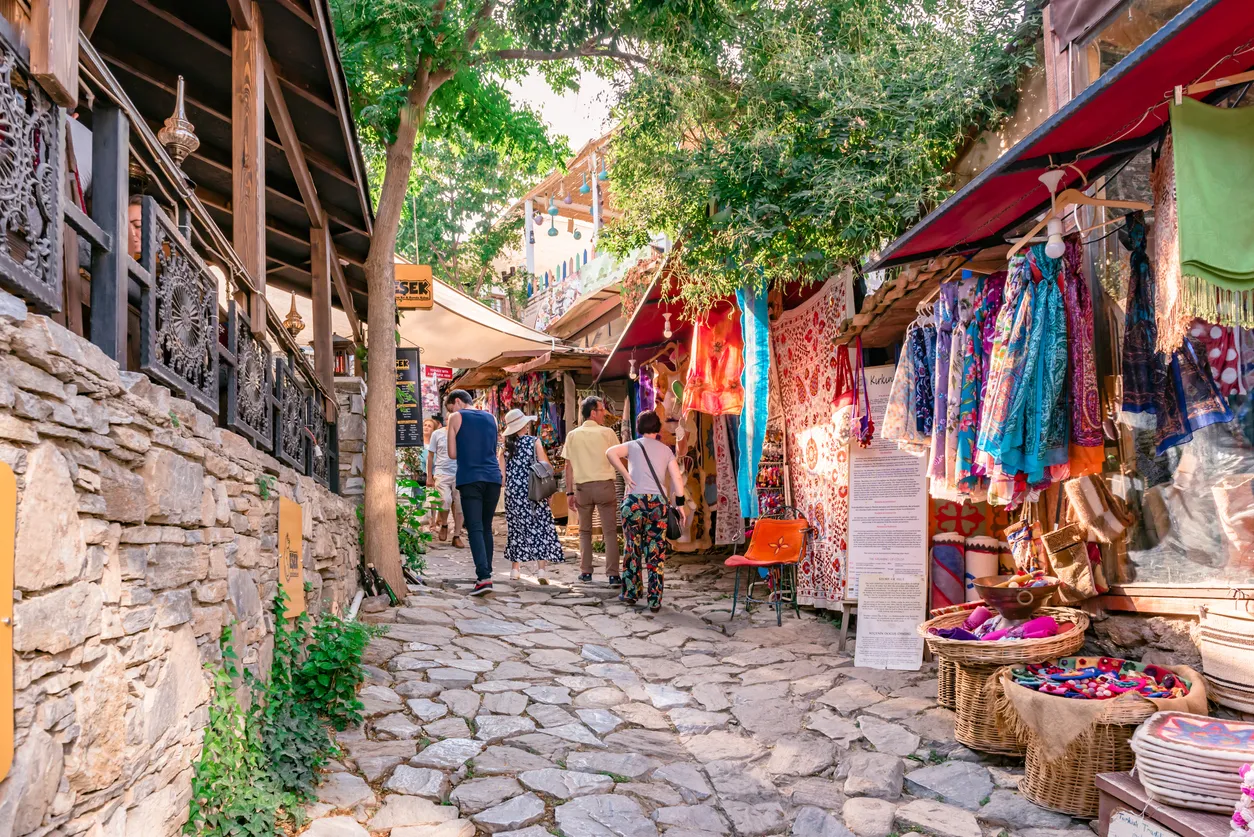 İzmir'in Şirince köyünde, Arnavut kaldırımlı tarihi bir sokağın iki yanında sıralanmış, yemyeşil sarmaşıklarla bezeli ve renkli çiçek saksılarıyla süslenmiş geleneksel taş evlerin gün batımına yakın saatlerdeki sıcak atmosferi.