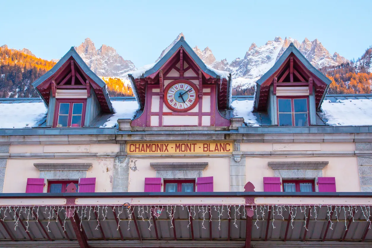 Chamonix Mont-Blanc tren istasyonunun cephesi, arka planda Fransız Alpleri ve güneş ışığıyla aydınlanan Mont Blanc zirveleri.