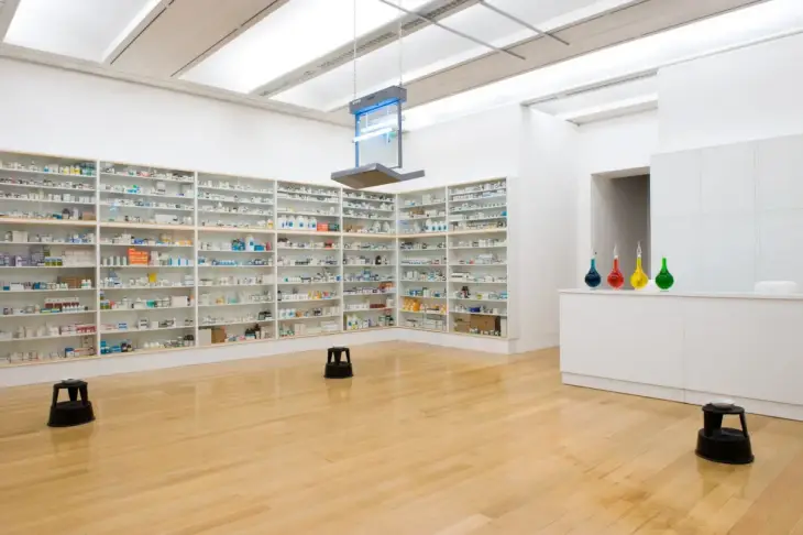 Damien Hirst’ün “Eczane” enstalasyonu – ilaç dolapları, neon ışık ve düzen saplantısı üzerinden modern yaşamın tıpla ilişkisini eleştiriyor.