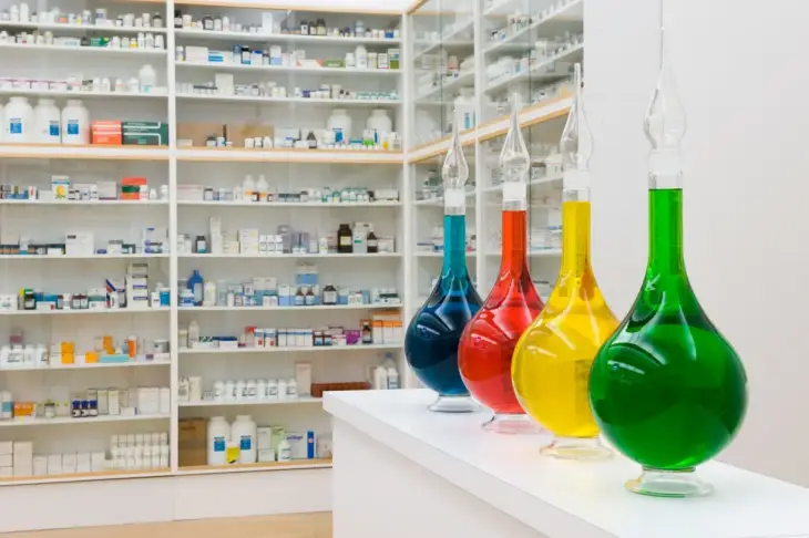 “Eczane” enstalasyonundan detay – kırmızı, mavi, sarı ve yeşil sıvı dolu kavanozlar, Damien Hirst’ün laboratuvar estetiğine göndermesi.