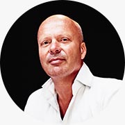 Mimar ve Brand Von Egmond markasının kurucusu William Brand'ın, Amsterdam gezi rehberi içeriğine özel olarak hazırlanmış, kel kafalı, beyaz gömlekli, kameraya samimi bir ifadeyle bakan portre fotoğrafı.