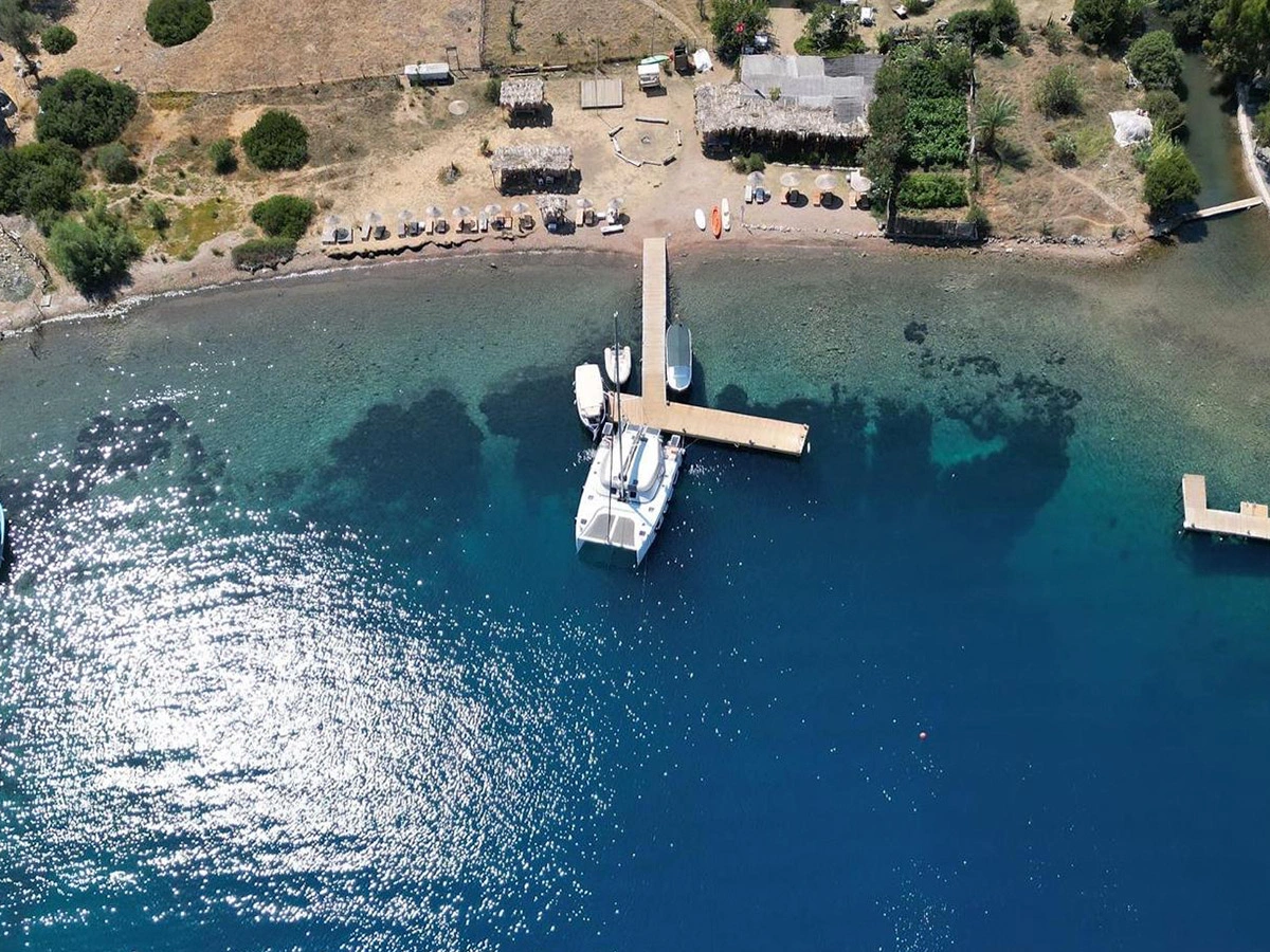 Kocabahçe Glamping'in tekneyle yanaşmaya uygun iskelesi ve berrak turkuaz deniziyle çevrili, güneşin pırıl pırıl yansıdığı kıyı şeridinin kuşbakışı görünümü, mavi yolculuk tutkunları için ideal bir durak olan bu saklı koyu gözler önüne seriyor.