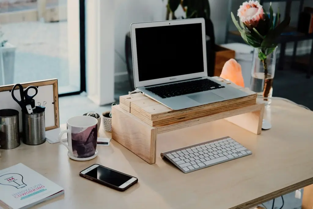 Düzenli çalışma masasında laptop standı, klavye, kahve fincanı ve çiçek: verimli çalışma alanı düzenleme ve ergonomi ipuçları.