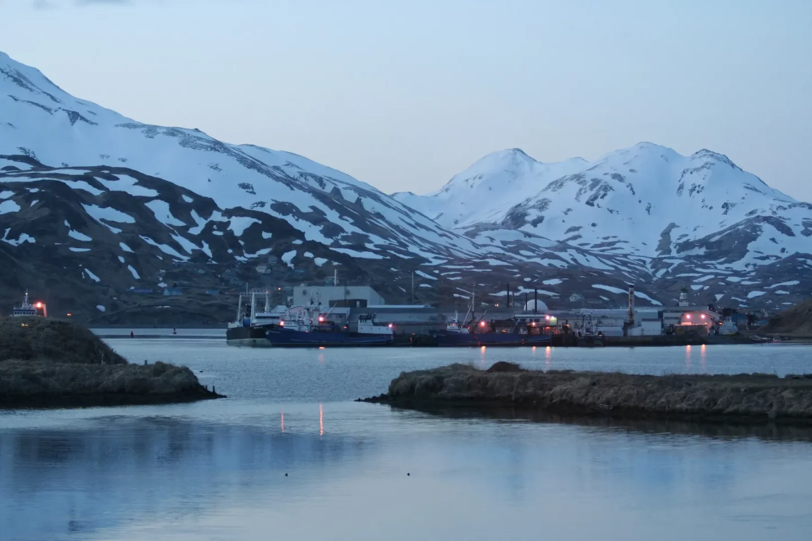 Kardan tepeleriyle dağların çevrelediği, alacakaranlıkta ışıkları suya yansıyan bir limanda, demirli balıkçı tekneleri ve endüstriyel yapılarla Alaska Dutch Harbor'daki bu manzara, Göksen Körezlioğlu'nun denize olan tutkusunu ve hayalindeki mavi yolculuk rotasını yansıtıyor.