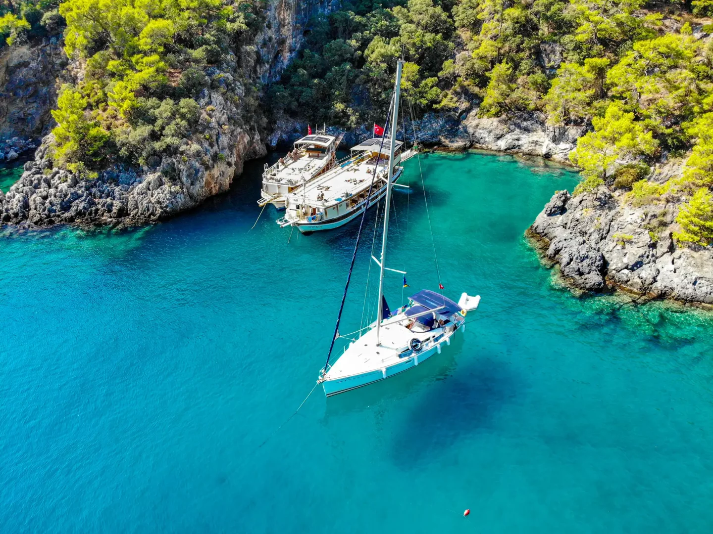 Kerem Görsev'in deniz tutkusunu yansıtan ve mavi yolculuk ruhunu barındıran bu büyüleyici hava fotoğrafında, yemyeşil ağaçlarla bezeli kayalıkların kucakladığı berrak turkuaz bir koyda, açık mavi, mavi ve lacivert tonlarının görüldüğü derin sularda iki teknenin huzurla demirlemesiyle oluşan eşsiz bir Akdeniz manzarası.
