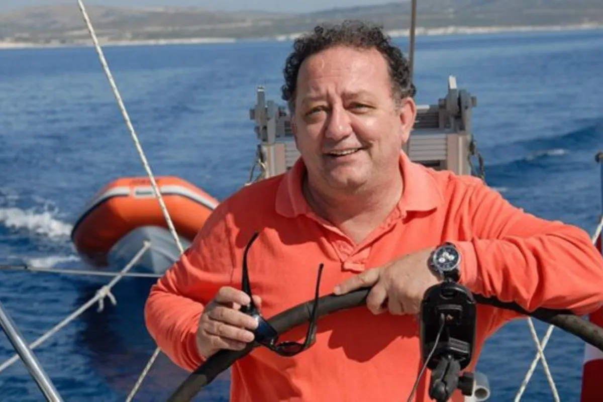 Denizcilik dünyasının önemli isimlerinden Meriç Köyatası, teknesinin dümeninde, üzerinde turuncu bir polo yaka tişörtle gülümsüyor, bir elinde tuttuğu güneş gözlüğü ve arkasındaki masmavi Ege denizi, turuncu renkte bir filika ve uzak kıyı şeridiyle mavi yolculuk tutkusunun ve denizle iç içe yaşam biçiminin adeta bir yansıması.