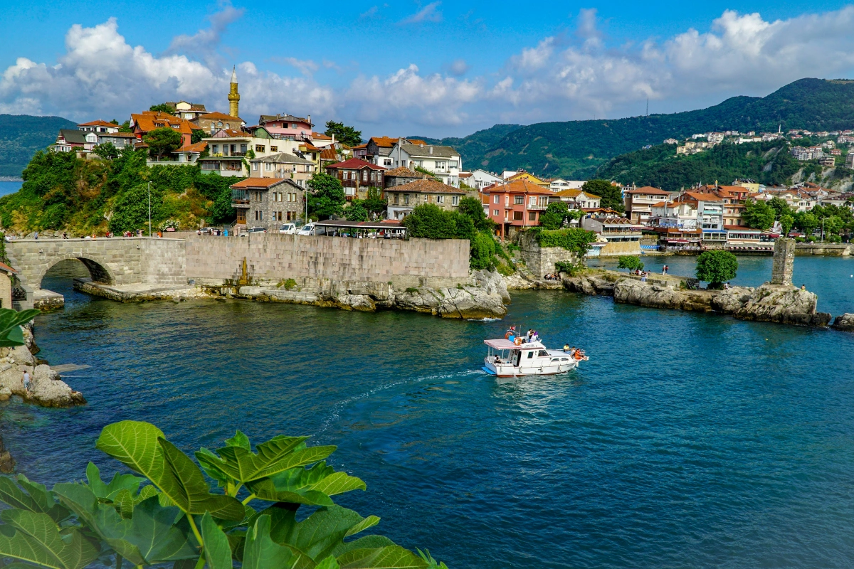 Karadeniz kıyısında yer alan Amasra'nın tarihi yarımadasını ve taş sokaklarını gözler önüne seren bu geniş açılı çekimde, yemyeşil tepelerin eteklerine sıralanmış rengarenk çatılı evler, antik bir taş köprü ve berrak mavi sularda ilerleyen küçük bir tekne, Türkiye road trip rotalarından Batı Karadeniz Sahil Yolu'nun sakin güzelliğini vurguluyor.