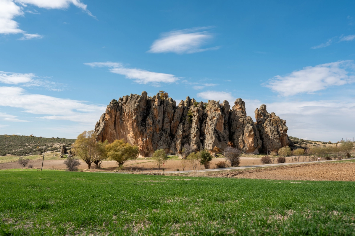Frig Vadisi'ndeki bir road trip sırasında görülen, yemyeşil otlarla kaplı ön plandaki alan ve kahverengi ekili toprağın ötesinde yükselen, gökyüzüne doğru sivrilen devasa kaya oluşumları, Anadolu'nun binlerce yıllık tarihini ve doğal manzaralarını yansıtıyor.