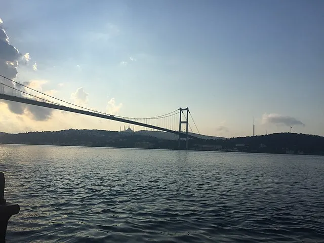 Boğaziçi Köprüsü’nün gün batımı ışığında Boğaz’dan görünümü, arka planda Çamlıca Camii ve Çamlıca Kulesi siluetiyle İstanbul manzarası