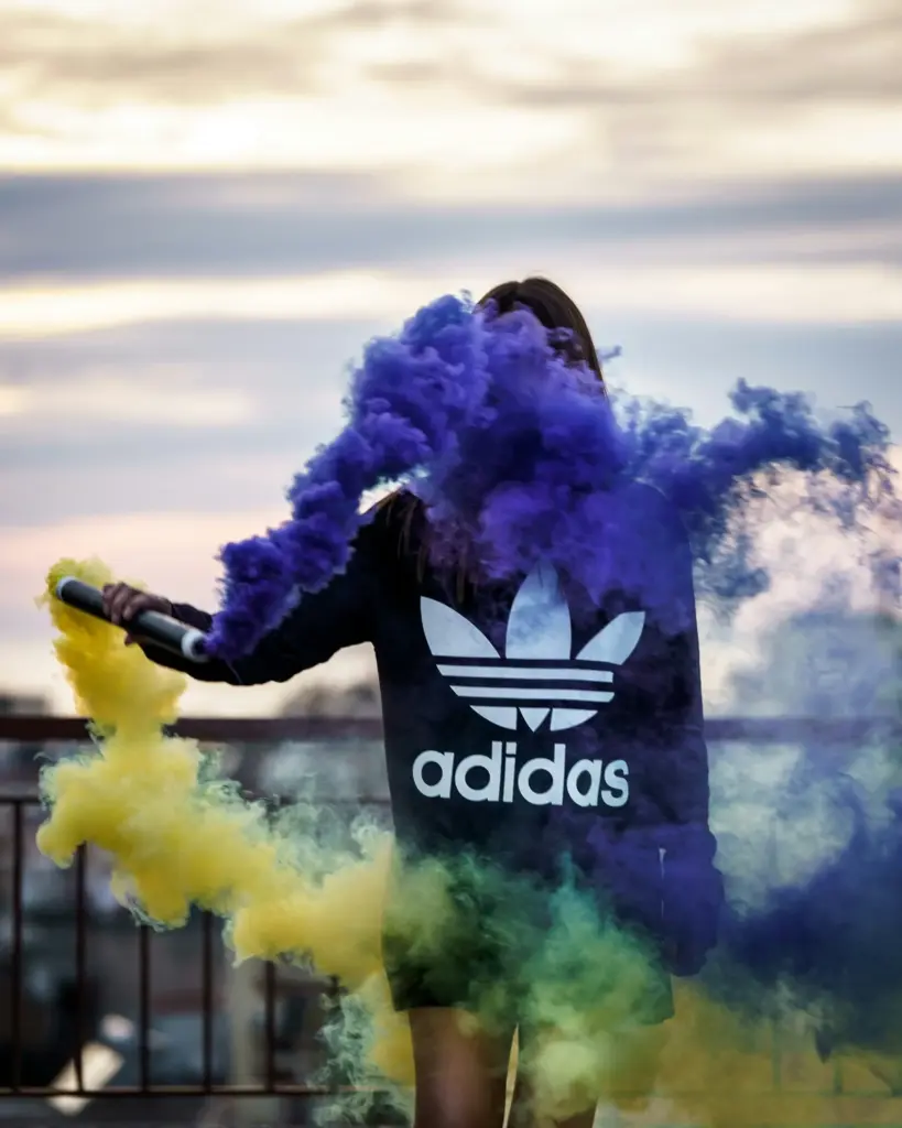 Renkli duman efektleriyle poz veren siyah Adidas sweatshirt giyen kişi