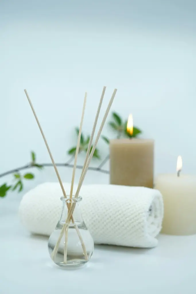 Aromaterapi çubukları, yakılmış mumlar ve beyaz havluyla spa ve wellness konseptinde rahatlatıcı bir atmosfer.