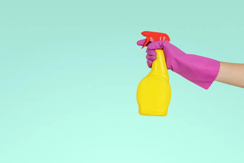 Pembe temizlik eldiveni takan elin tuttuğu sarı sprey şişesiyle hijyen ve dezenfeksiyon
