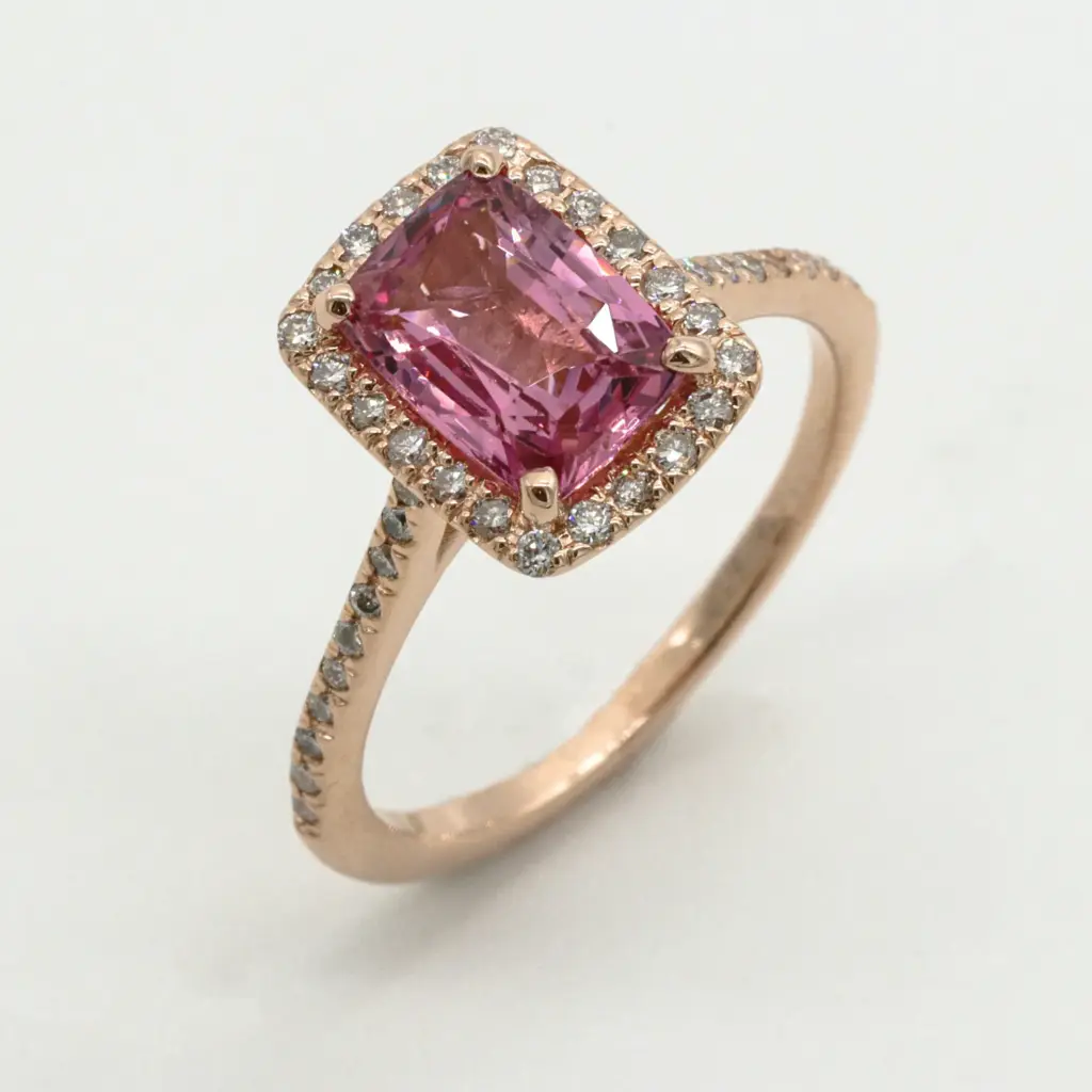 Pembe yastık kesim değerli taşla süslenmiş, etrafı küçük pırlantalarla çevrili ve ince taşlı şerit tasarıma sahip altın yüzük.