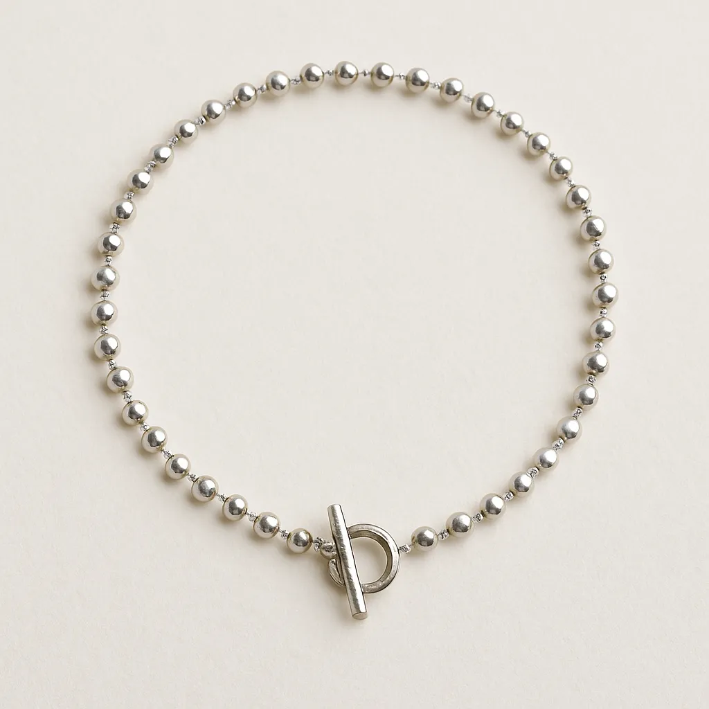 Yuvarlak metal boncuklardan oluşan, önde halka ve çubuk şeklinde toka detayı bulunan gümüş renkli choker kolye.