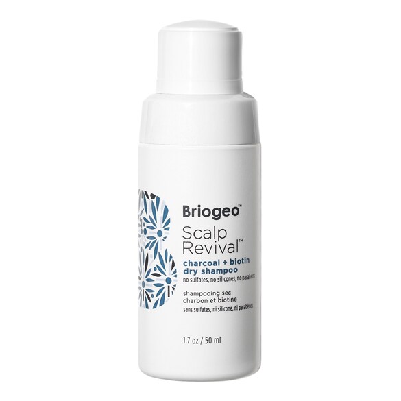 Beyaz bir arka plan üzerinde duran, üzerinde Briogeo Scalp Revival charcoal + biotin dry shampoo yazan beyaz silindirik şişe, saç derisindeki kirleri temizleyip fazla yağı emerek saça temiz, ferah ve hacimli bir his veren en iyi kuru şampuanlardan birini gösteriyor.