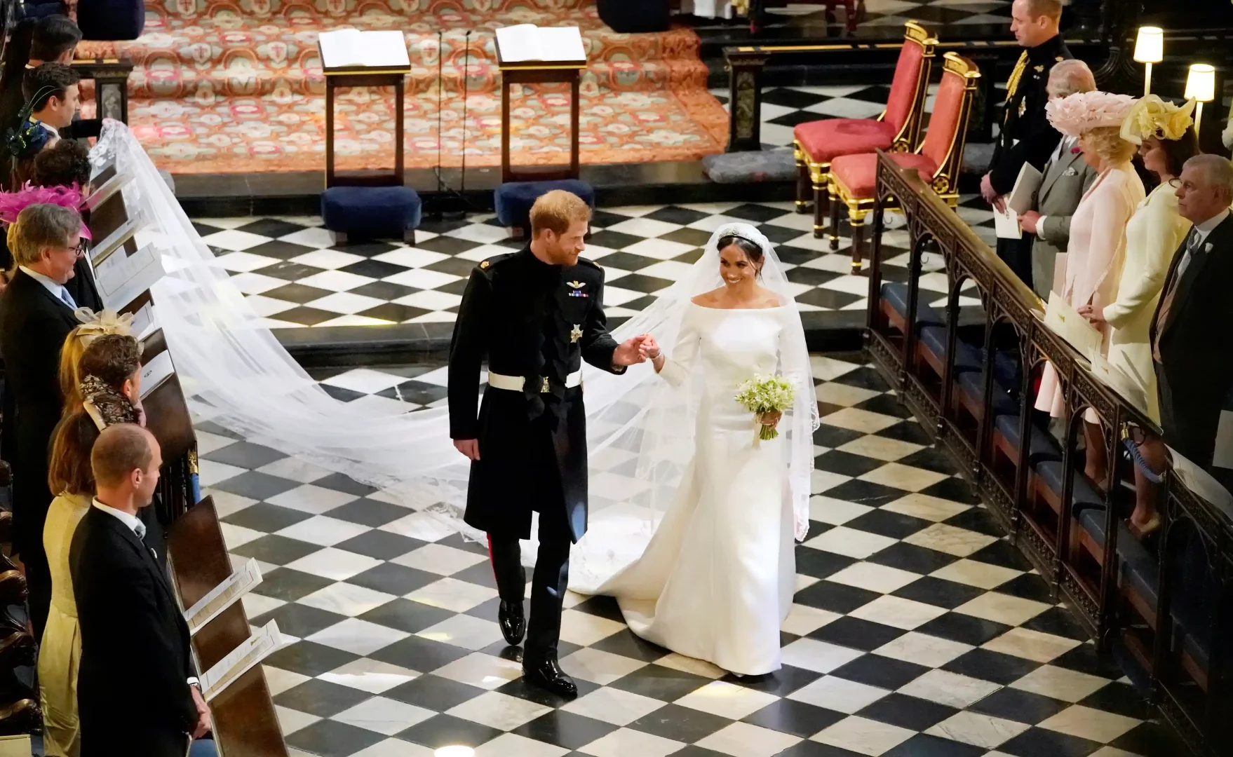Prens Harry ile el ele kilise koridorunda ilerlerken, sade ve omuzları açık minimalist gelinliği, uzun ve zarif duvağıyla ışıldayan Meghan Markle, moda tarihine damga vuran unutulmaz gelinliklerden birini giyerek ikonik bir an yaratıyor.