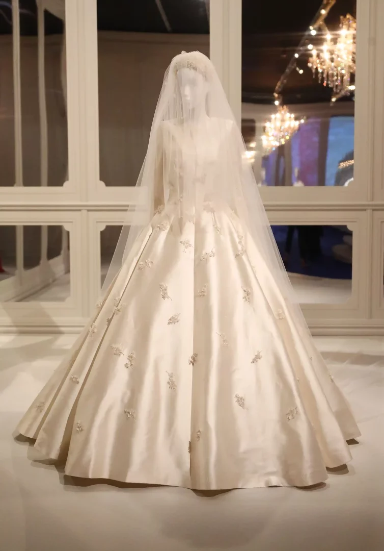 Mannequin üzerinde sergilenen, Grace Kelly gelinliğinden ilham alan Miranda Kerr'in fildişi rengi, yüksek yakalı, uzun kollu ve hacimli etekli gelinliği, eteklerinde dağınık zarif işlemeler ve taçlı uzun tül detaylarıyla dikkat çekiyor, unutulmaz gelinlikler arasında yer alıyor.