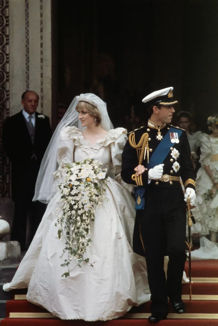 1981'de St. Paul Katedrali'ndeki kraliyet düğününde Prens Charles ile merdivenlerden inen Prenses Diana, kabarık kollu, fırfırlı ve uzun duvaklı masalsı gelinliği içinde, elinde beyaz sarkık çiçeklerden oluşan gösterişli buketiyle büyüleyici görünüyor.