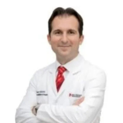 Beyaz önlük ve kırmızı kravatıyla poz veren Kadın Hastalıkları ve Doğum Uzmanı Dr. Üzeyir Kalkan; Koç Üniversitesi Hastanesi'nde görev yapan jinekolojik endoskopik cerrahi uzmanı profesyonel portresi.