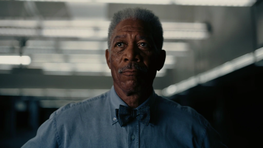 Morgan Freeman, The Dark Knight filminde Lucius Fox rolünde ciddi bir bakışla teknoloji dolu bir ortamda dururken zekâyı ve stratejiyi temsil ediyor.