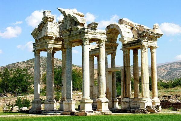 Aydın'ın Karacasu ilçesinde yer alan UNESCO Dünya Mirası Listesi'ndeki Afrodisias antik kentinde, yemyeşil bir zeminde yükselen, beyaz mermer sütunları ve yer yer yıkılmış kısımlarıyla geçmişin görkemini bugüne taşıyan, etkileyici bir antik yapı fotoğrafı.