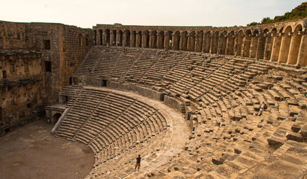 Türkiye’nin eşsiz antik kentlerinden Aspendos’ta yer alan, bir kişinin ölçeğini gösterdiği sahne zemininden yukarı doğru yükselen basamakları ve kemerli sahne binasıyla günümüze dek en iyi korunmuş, harika akustiğe sahip görkemli Roma tiyatrosu.