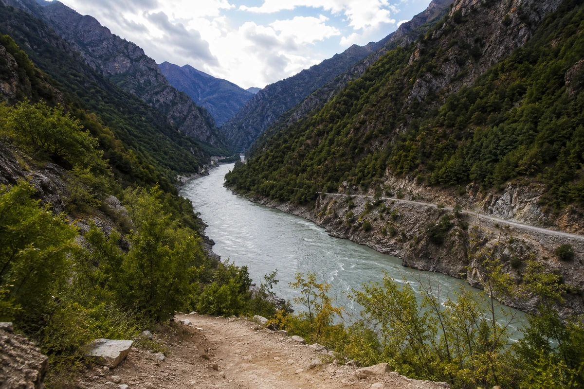 Artvin'deki Çoruh ekoturizm alanının görkemli doğasını gözler önüne seren bu geniş açılı manzara, coşkun Çoruh Nehri'nin yemyeşil ve sarp dağ yamaçları arasında kıvrılarak akışını, ön plandaki toprak patika ile uzaklardaki dağ yolunu ustalıkla birleştiriyor.