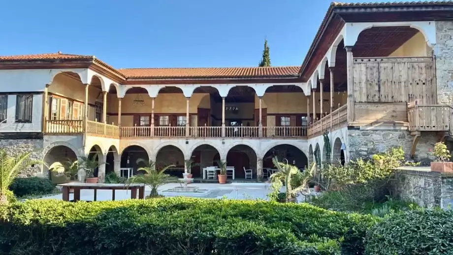 Avlulu, kemerli geçitleri ve ahşap detaylarla süslenmiş balkonları olan, taş ve sıva karışımı duvarlara sahip, iki katlı, geleneksel Türk mimarisini yansıtan bu tarihi yapı, yemyeşil bitkilerle çevrili huzurlu bir atmosfer sunuyor.