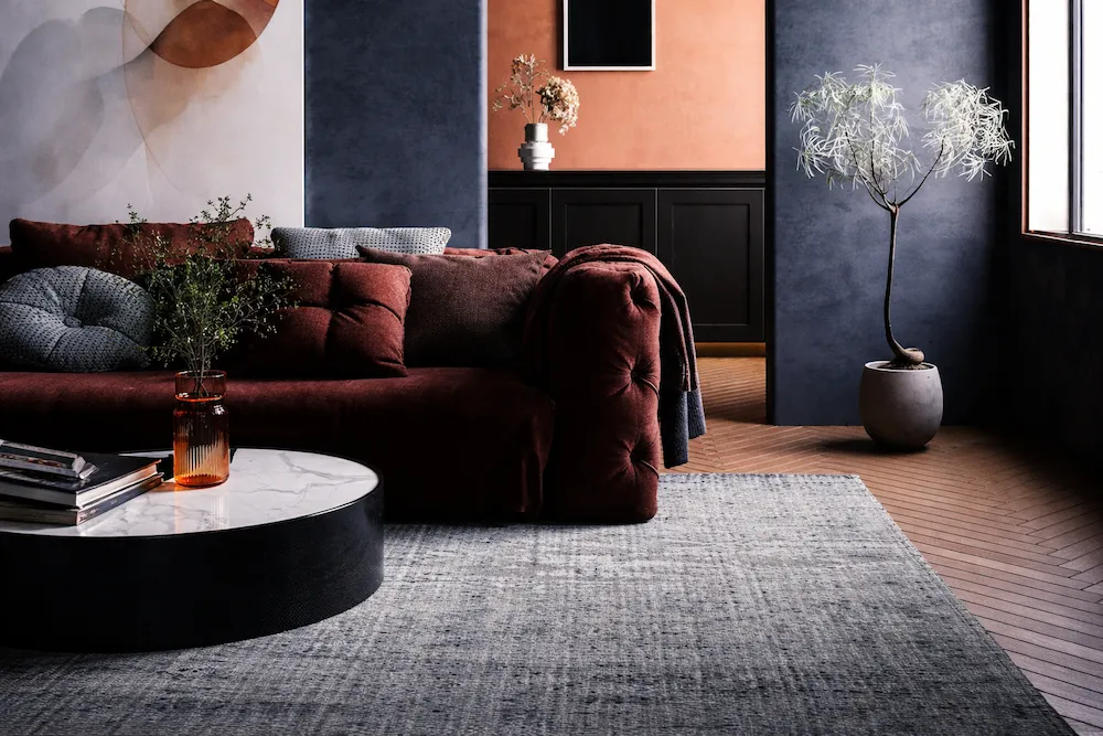 Modern lüks salon dekorasyonu; bordo kadife koltuk, mermer sehpa, koyu lacivert ve toprak tonlarında duvarlar, katmanlı dokular ve sofistike aydınlatma ile zengin renk–malzeme uyumu sunan iç mekân tasarımı.