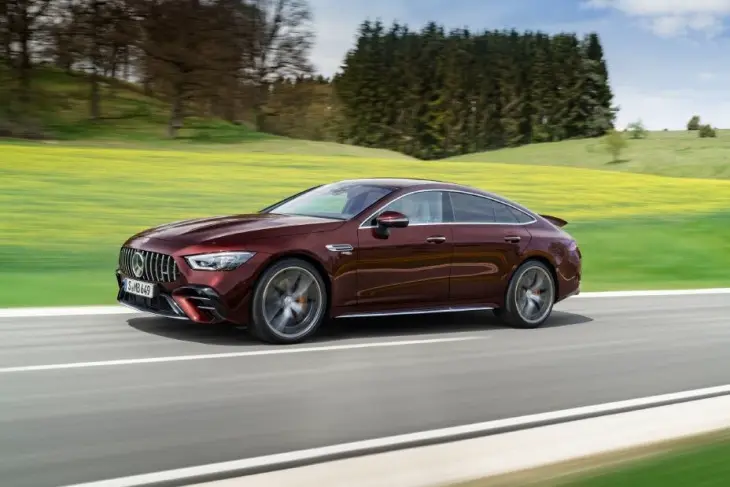Geniş yeşil bir arazideki asfalt yolda hızla ilerleyen koyu bordo renkli Mercedes-AMG GT 4 Kapı Coupe, performans ve lüksü bir araya getirerek hem sportif sürüş deneyimi hem de dört kişilik yaşam alanı arayanlara hitap eden çağdaş tasarımını sergiliyor.