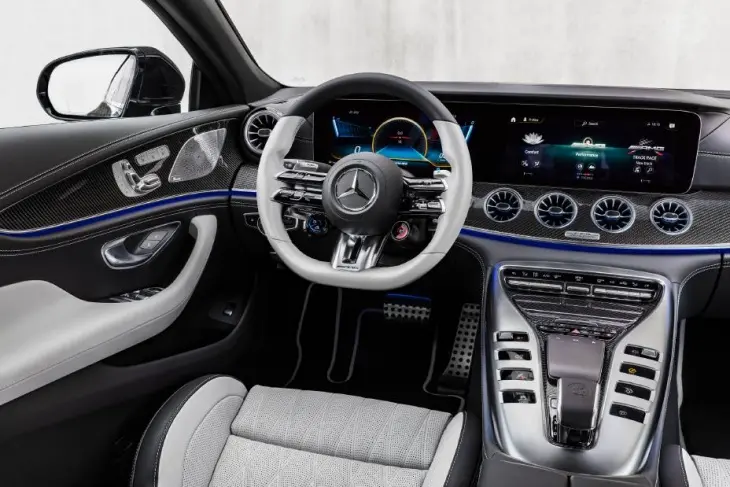 Bu Mercedes-AMG GT 4 Kapı Coupe'nin sportif ve teknolojiyle dolu iç mekanında, beyaz ve siyah detaylara sahip direksiyon simidi, çift dijital ekran, karbon fiber kaplamalar ve mavi ambiyans aydınlatması lüks performansı vurguluyor.