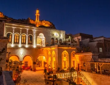 Gece karanlığında, tepesinde belirgin bir minaresi olan geleneksel taş mimarili tarihi bir Selçuklu oteli, kemerli pencereleri ve alt kattaki geniş avlu benzeri alanları sıcak sarı ışıklarla aydınlatılarak büyüleyici bir atmosfer sunuyor.