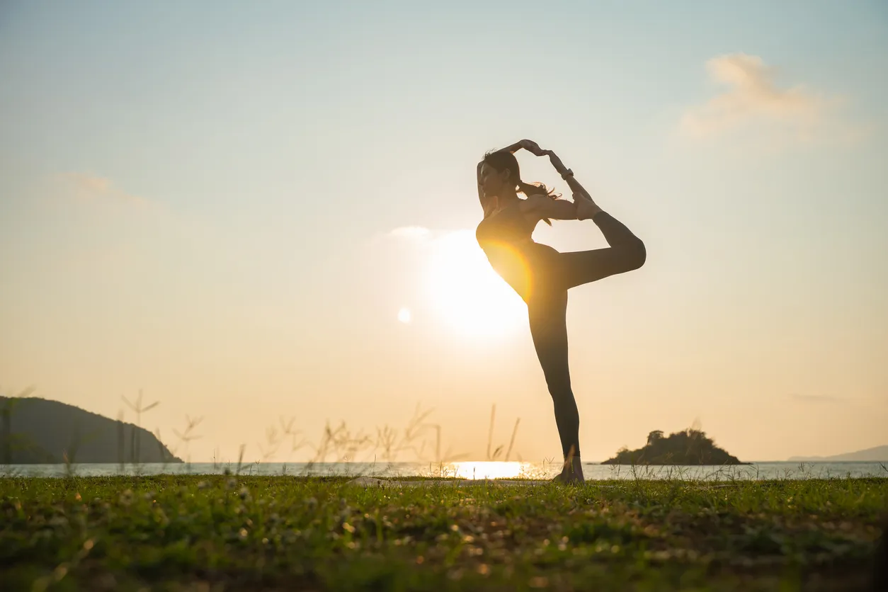 Gün batımının huzurlu ışığında deniz kenarında yoga duruşu yapan bir kadının silueti, vagus sinirinin aktivitesini artırarak yaşam kalitesini iyileştirme ve stresi azaltma potansiyelini vurguluyor.