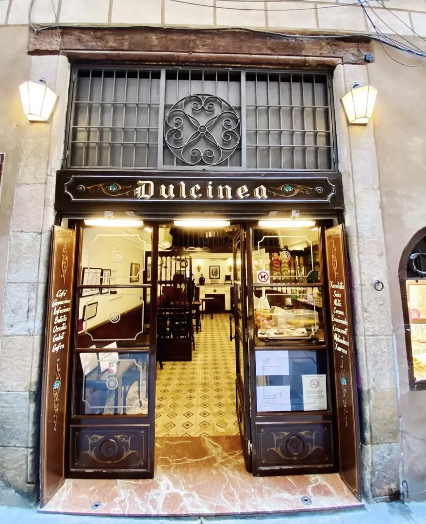 Dulcinea adlı, ahşap ve cam detaylı süslü çift kanatlı kapıları sonuna kadar açık, iç mekanında geometrik desenli fayans zemin ve masaların görüldüğü geleneksel bir kafenin ön cephesi; üst kısmında ferforje detaylı bir pencere ızgarası ve iki yanında sıcak ışık yayan fenerlerle dikkat çekerken, kapı camlarındaki menüde churros, orxata ve çeşitli çikolatalar gibi granja lezzetleri listeleniyor.