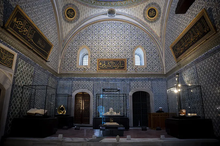 Topkapı Sarayı'ndaki Kutsal Emanetler Dairesi'nin mavi ve beyaz desenli çinilerle süslü, hat yazıları ve yuvarlak madalyonlarla zenginleştirilmiş tavan ve duvarlarına sahip geniş odasında, cam vitrinlerde sergilenen el yazması kitap, altın rengi nesne ve diğer dini eserler dikkat çekiyor.