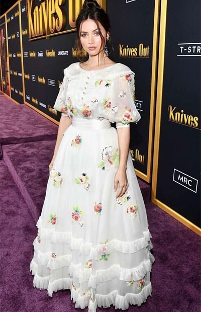 Ana de Armas, mor bir halıda, kabarık kollu, önü düğmeli, saten kemerli, pastel renkli çiçek desenleriyle süslü beyaz fırfırlı uzun organze elbisesi ve dağınık topuzuyla romantik stilini gözler önüne seriyor.