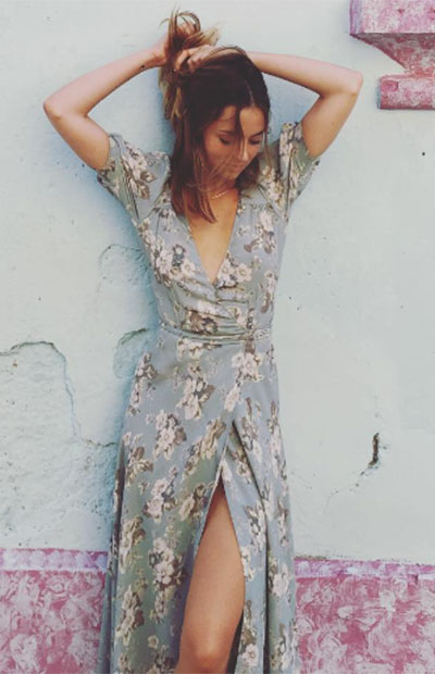 Ana de Armas, saçlarını toplarken, V yaka ve yırtmaç detaylı, uçuşan kumaşlı, açık mavi floral desenli elbisesiyle doğal ve romantik bir stil sergiliyor, bu görünüm onun gündelik stil rehberinden bir kesit sunuyor.
