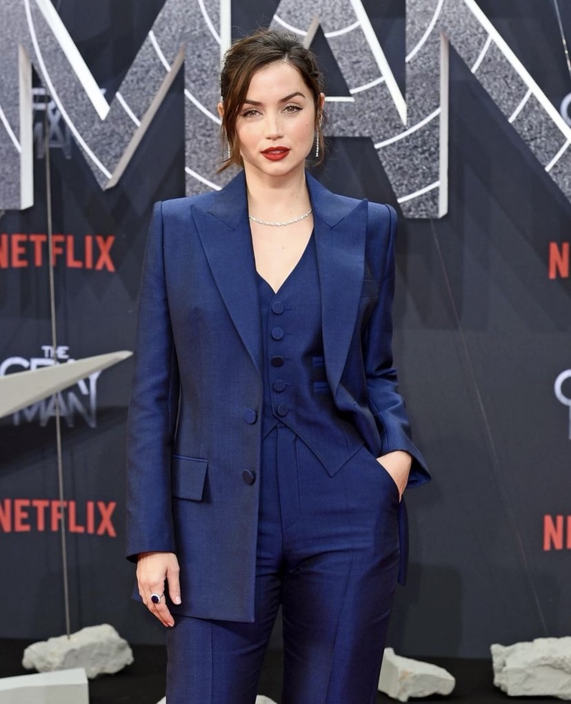 Ana de Armas, The Gray Man filminin Berlin prömiyerinde giydiği lacivert üç parçalı takım elbisesiyle maskülen ve zarif stilini gözler önüne seriyor; uzun blazer ceketi, düğmeli yeleği ve pantolonuyla kombinlediği görünümünü ışıltılı elmas kolye, damla küpeler ve belirgin koyu kırmızı rujuyla tamamlayarak kameraya bakıyor.
