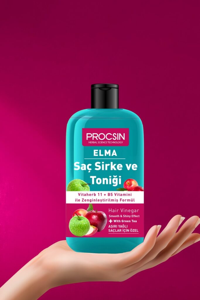 Koyu pembe bir arka plan önünde, bir elin tuttuğu, Vitaherb 11 + B5 vitamini ile zenginleştirilmiş, aşırı yağlı saçlar için özel olarak formüle edilmiş, üzerinde elma görselleri ve ELMA Saç Sirke ve Toniği yazan, turkuaz renkli bir PROCSIN şişesi.
