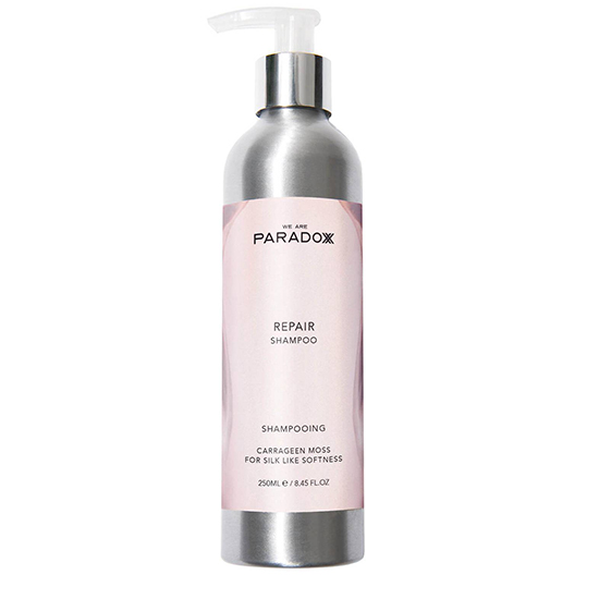 Ortada pembe etiketi olan, üstünde WE ARE PARADOXX markası ve REPAIR SHAMPOO yazan, ipeksi yumuşaklık için karagen yosunu içerdiğini belirten 250 ml'lik gümüş renkli metalik bir pompalı şişe sülfatsız şampuan, kuru ve yıpranmış saçları onararak parlaklık ve güç kazandırma vaadiyle sunuluyor.